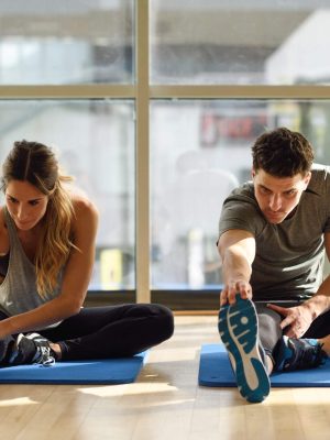 Young woman and man working out indoors. Two people streching their legs on the floor of a gym.